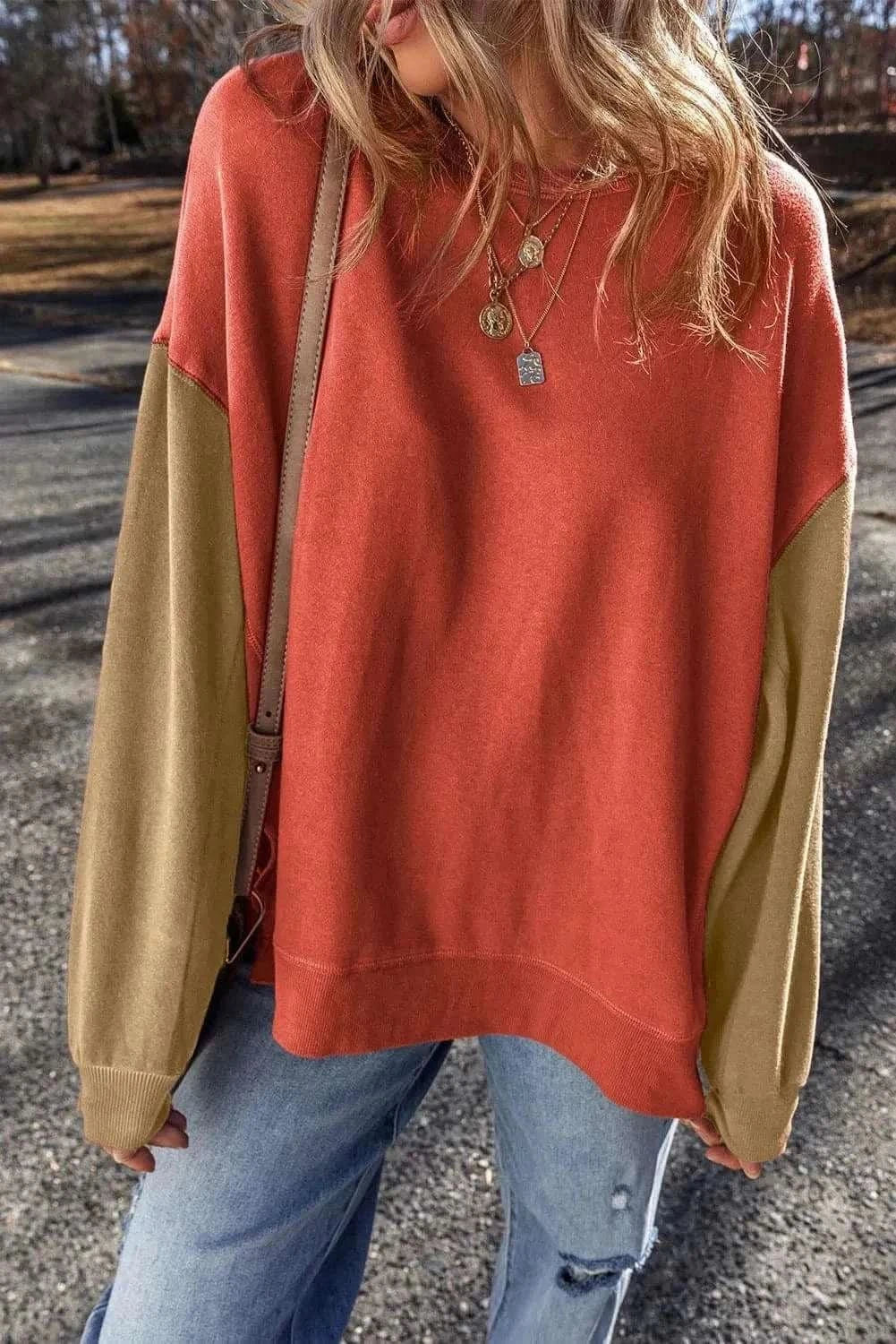 Color-blocked long sleeve sweatshirt in orange and olive tones, worn casually with jeans.