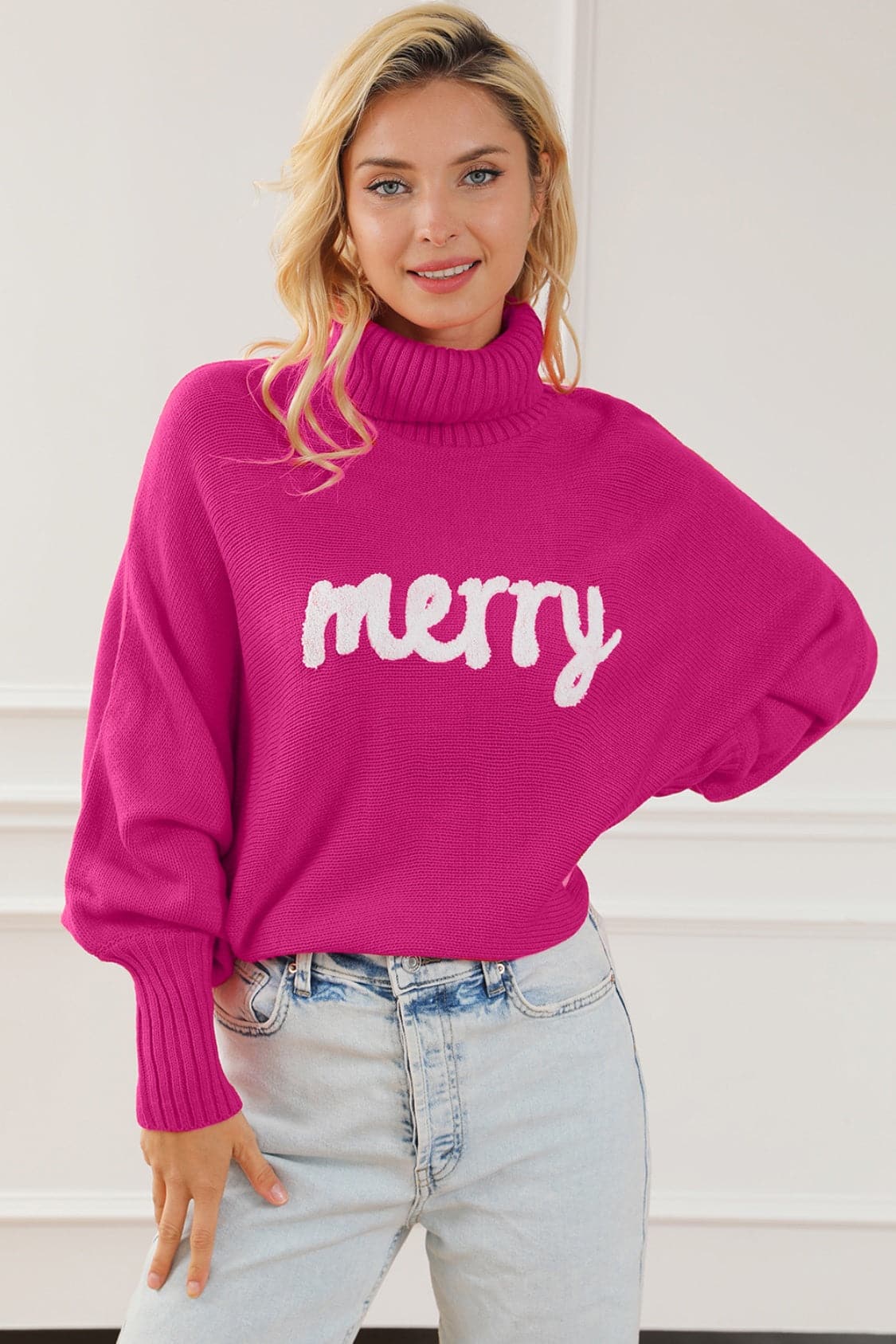 Cozy Merry High Neck Pullover in pink with white lettering, woman wearing casual jeans.