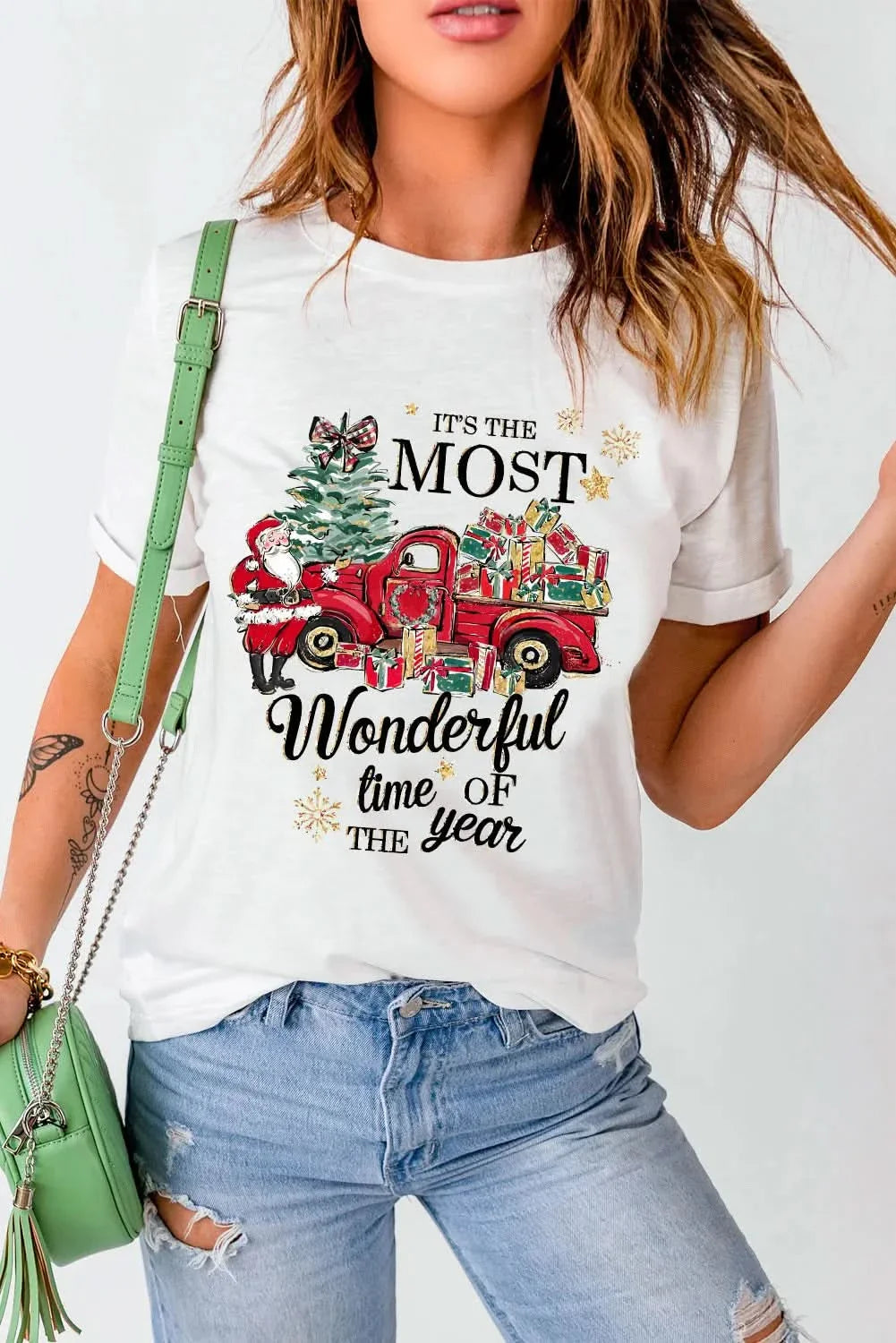 Graphic round neck short sleeve T-shirt with festive red truck design and text, paired with distressed jeans and a green bag.