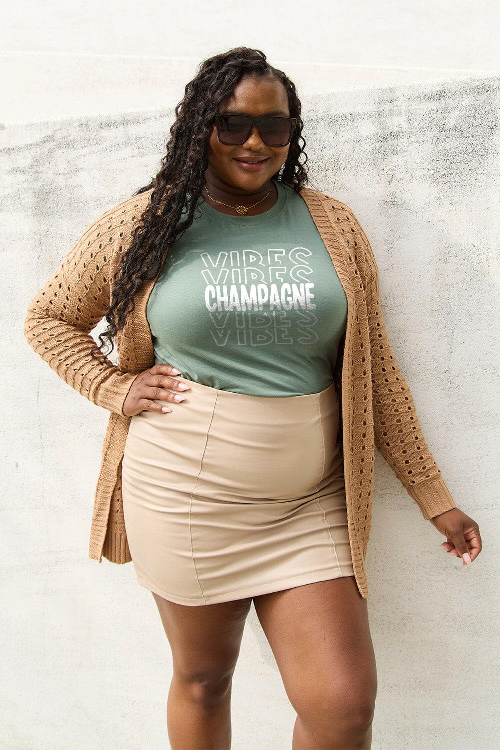 Plus-size woman wearing Champagne Vibes tee with cardigan and skirt, showcasing soft cotton and versatile style.