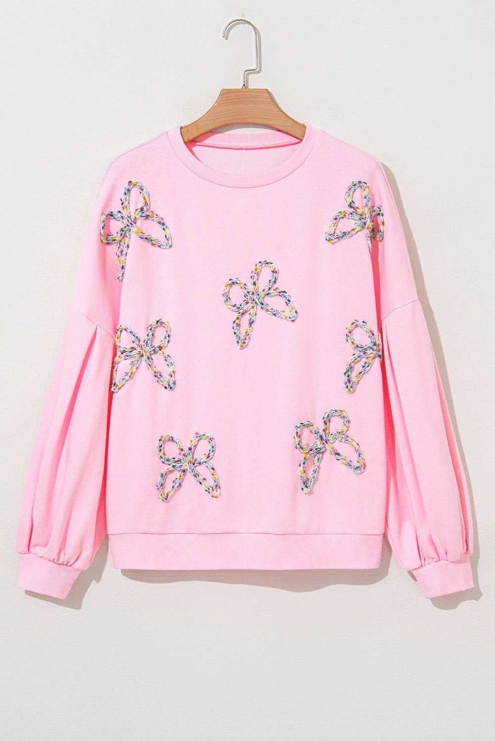 Light pink oversized pullover sweatshirt with embroidered bows and lantern sleeves.