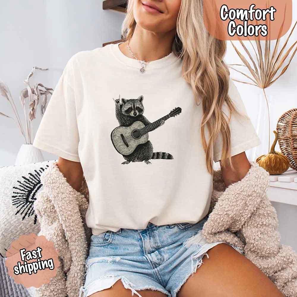 Adorb Custom Tees Raccoon T-shirt, a soft Comfort Colors funny animal shirt with a detailed guitar-playing raccoon.