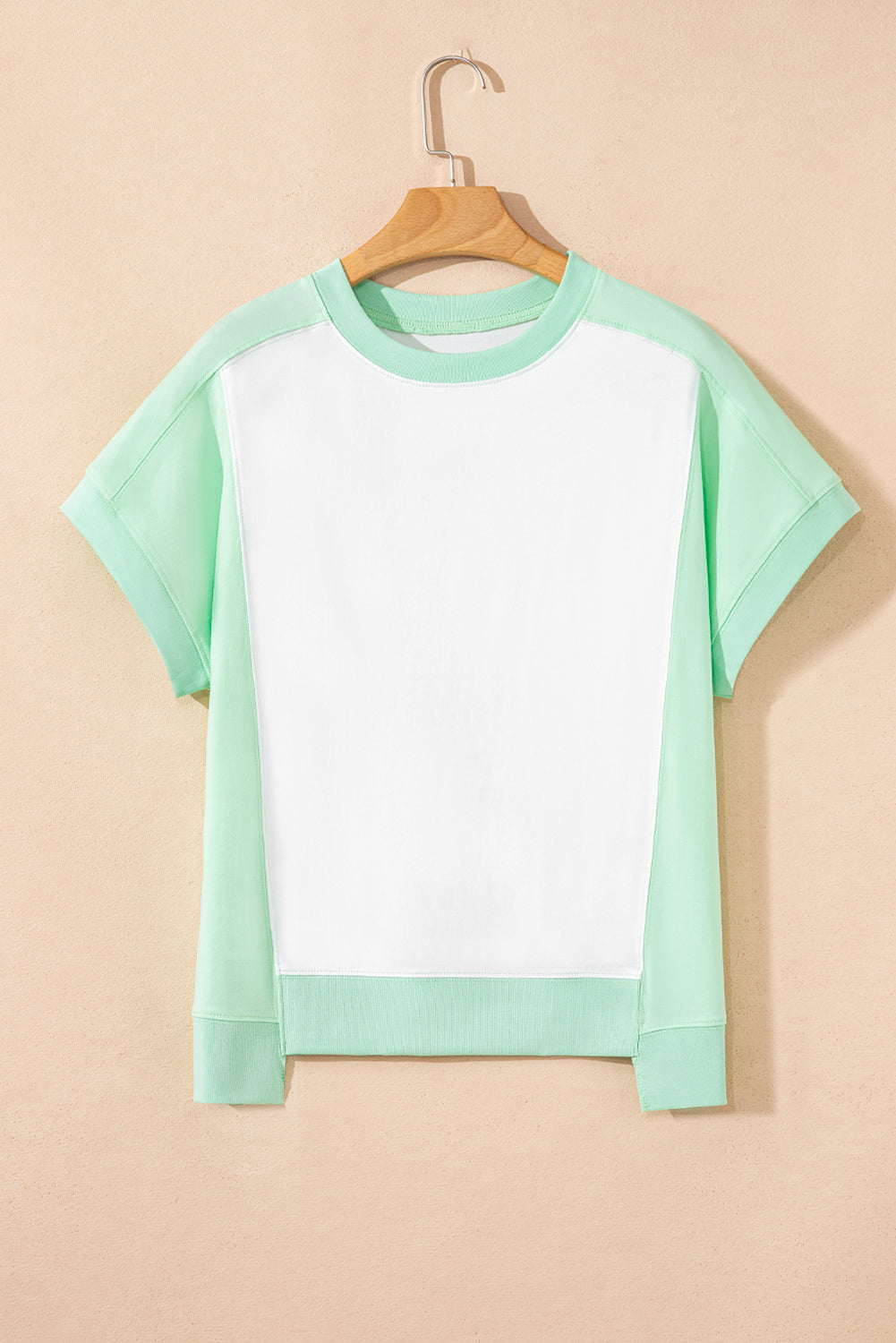 Light green color block exposed seam crew neck t-shirt hanging on a wooden hanger.