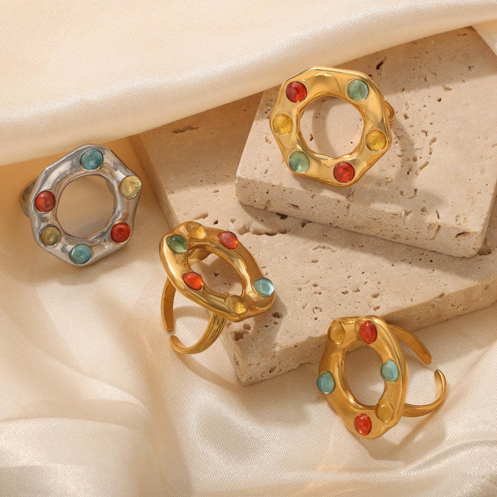 Titanium steel ring with colorful glass beads and gold-plated finish on neutral fabric background.