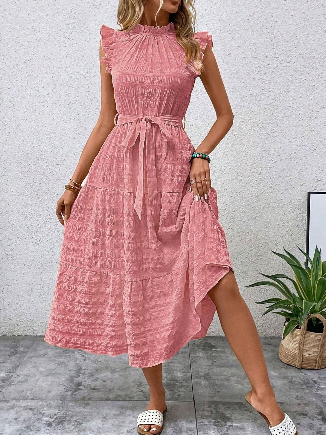 Pink ruffled cap sleeve midi dress with tie waist, worn by model, showcasing textured fabric.