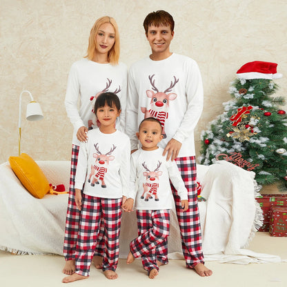 Family wearing matching Christmas pajamas with elk prints and plaid pants in festive living room setting.