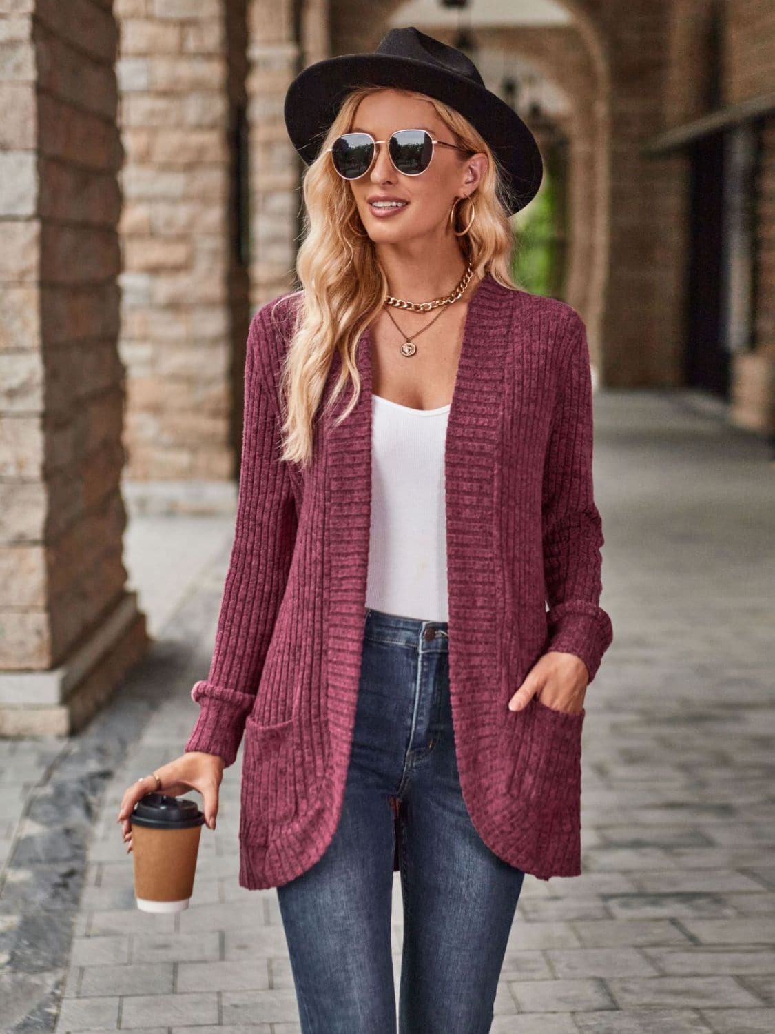 Cozy open front cardigan with pockets in maroon on a stylish model wearing jeans and a hat, holding a coffee cup.