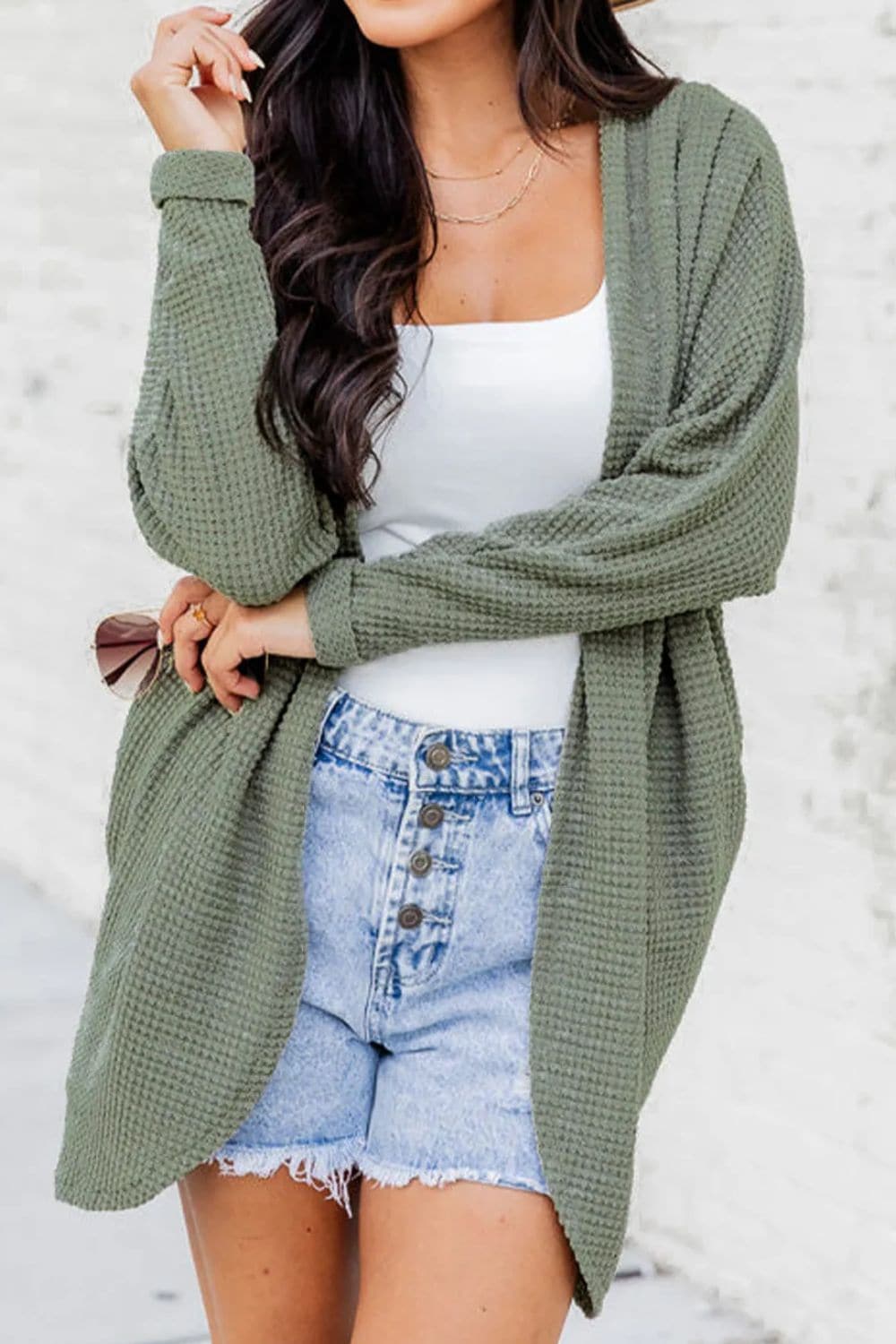 Cozy open-front cardigan with pockets in green, worn over a white top and denim shorts.