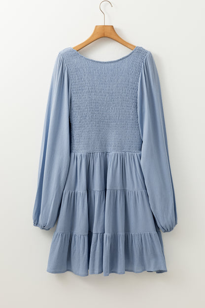 Ashleigh Blue smocked tiered mini dress with long sleeves and V-neckline.