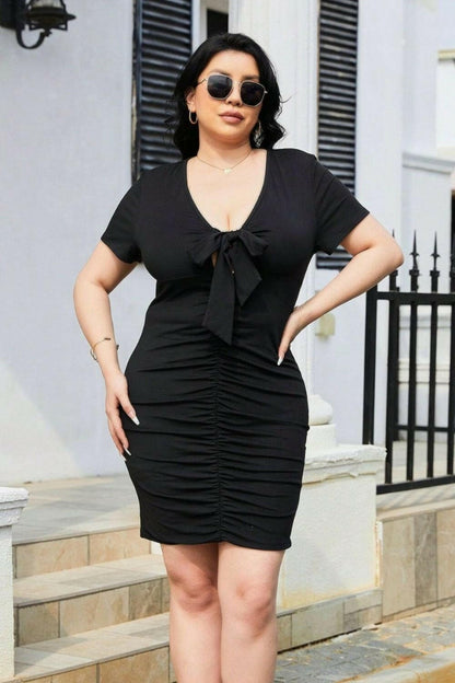 Plus size ruched mini dress with tie detail, black, short sleeves, flattering fit.